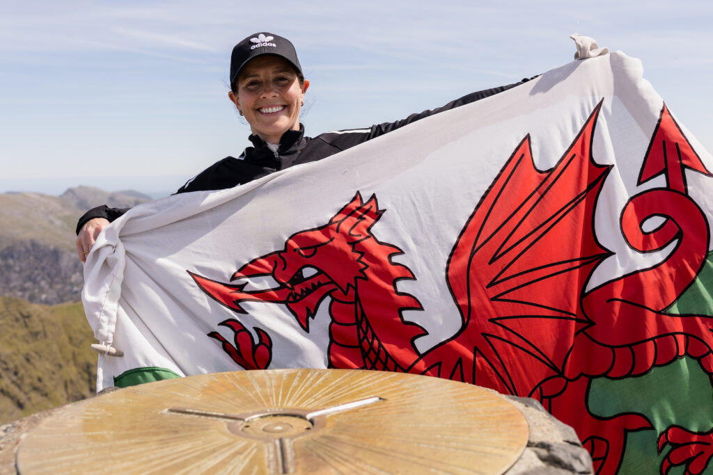 Rhian Wilkinson with a Wales flag on top of Wyddfa ahead of the UEFA EWRO Menywod 2025