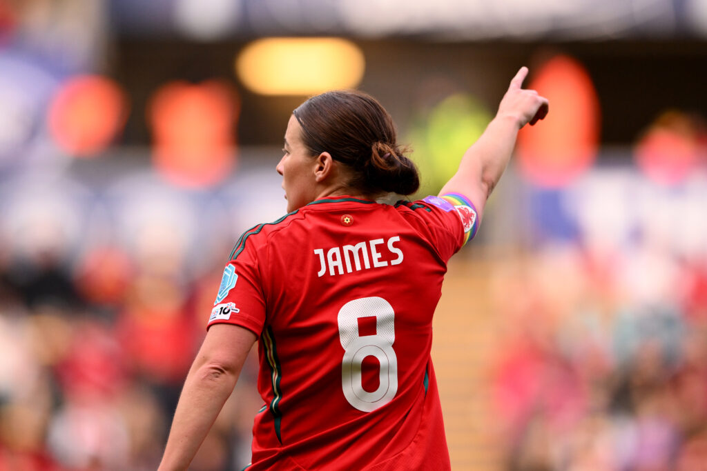 Angharad James with the Cymru squad numbers 8 playing for Wales with a rainbow captain's armband 
